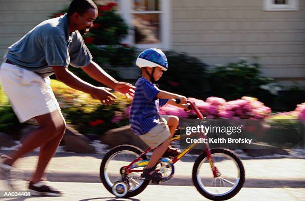 father teaching his son to ride on a bicycle - stützrad stock-fotos und bilder