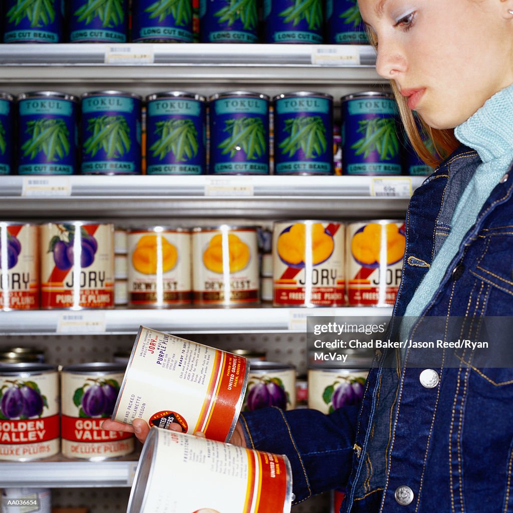 Teenage girl (14-16) looking at cans in supermarket, side view