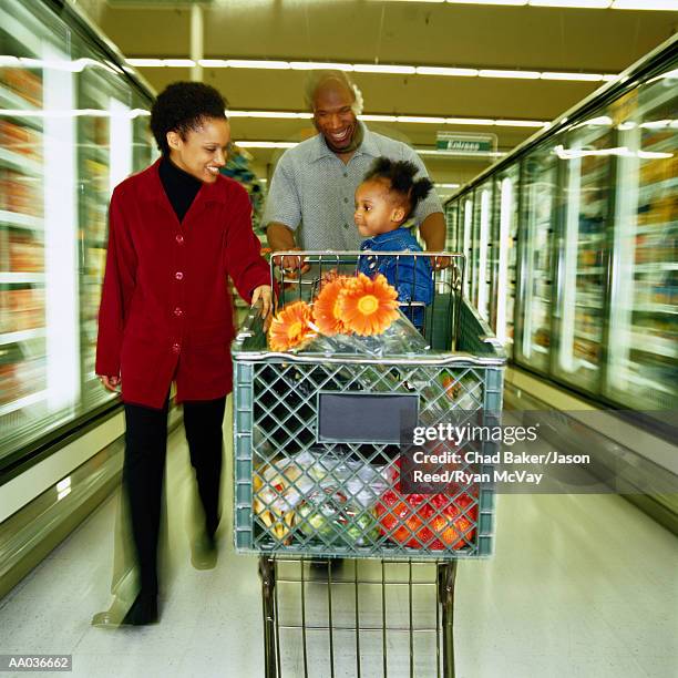 parents pushing toddler (21-24 months) in shopping cart at supermarket - full frontal stock-fotos und bilder