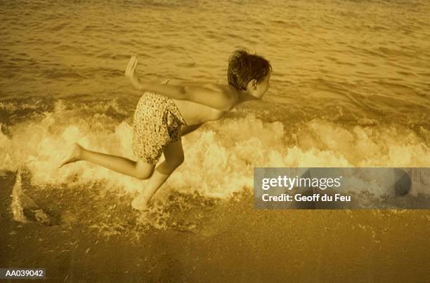 boy (6-8) playing in surf, side view (sepia tone) - du stock pictures, royalty-free photos & images