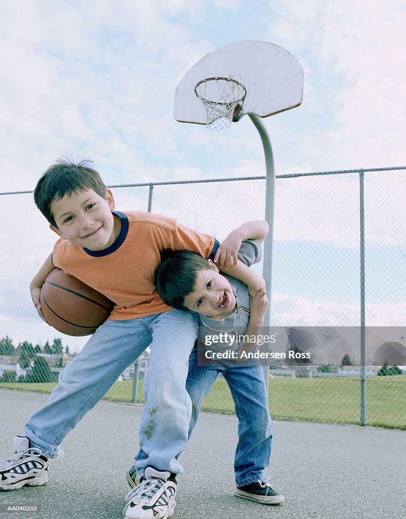 Two brothers (3-7) playing on basketball court, portrait