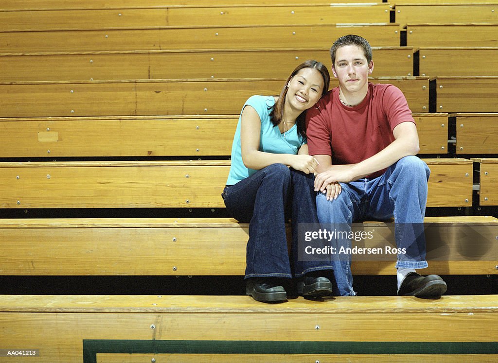 Teenage couple (15-17) sitting on school gym bleachers, portrait