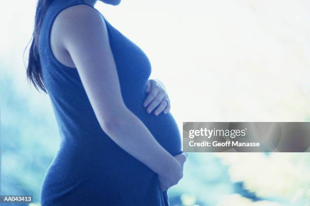 pregnant teenage girl (15-17) holding stomach, mid section, side view - embarazo de adolescente fotografías e imágenes de stock