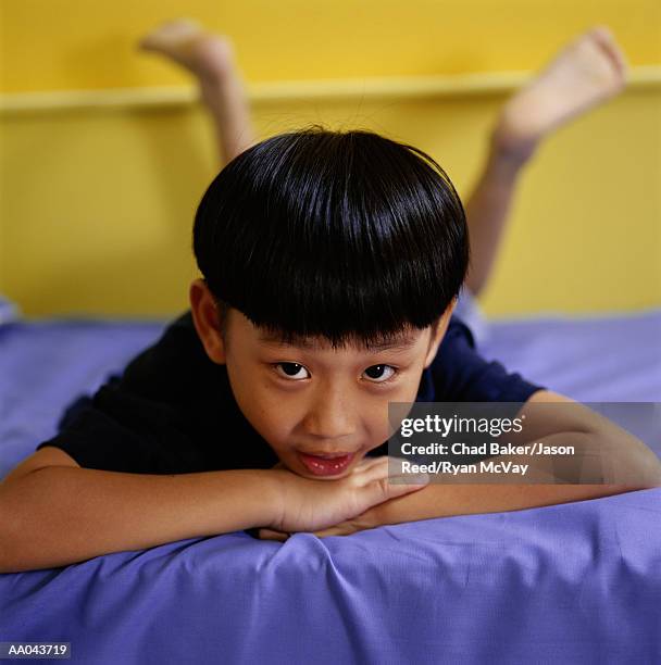 boy (7-9) lying on bed, resting chin on hands, portrait - reed bed stock pictures, royalty-free photos & images