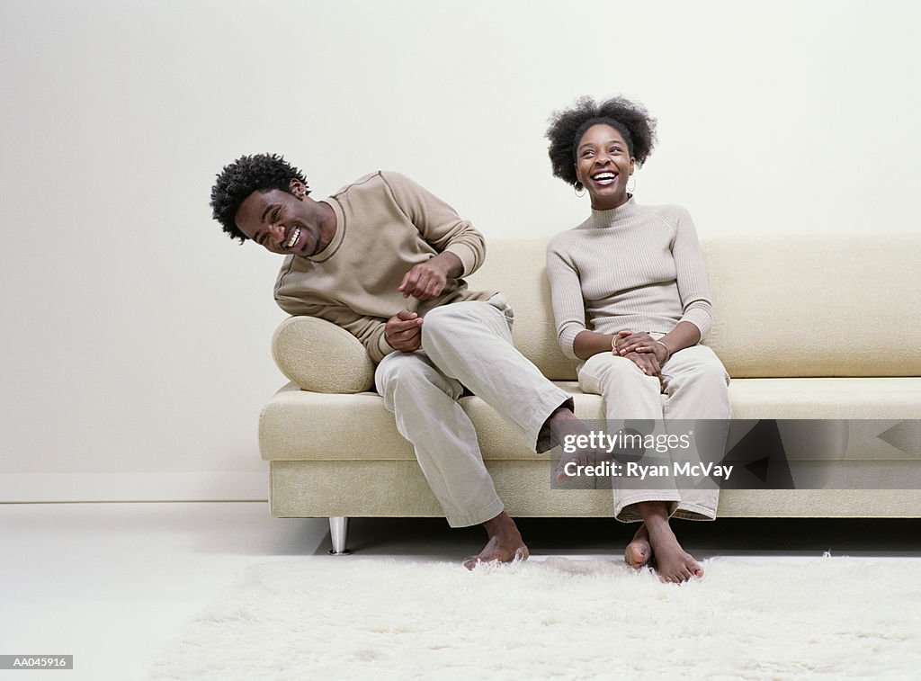 Young man and woman sitting on sofa, laughing