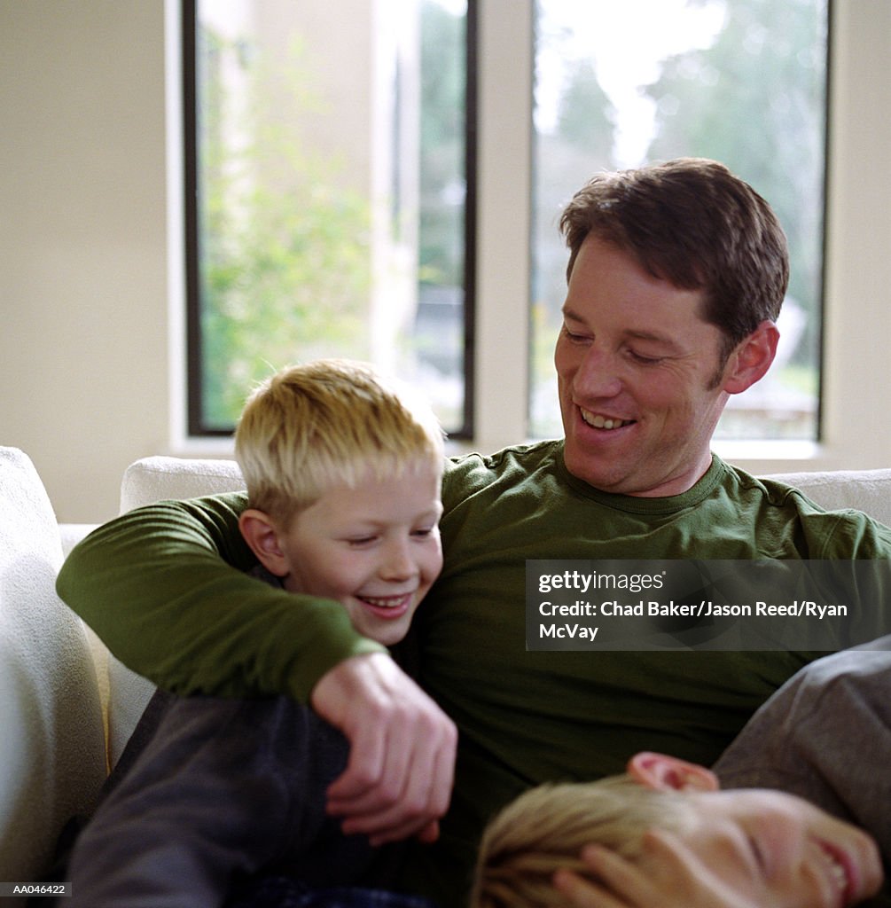 Father sitting on sofa with two sons (7-10), laughing