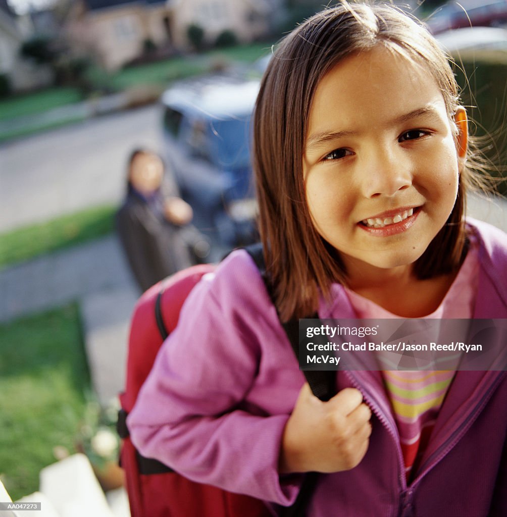 Girl (6-8) carrying backpack, smiling, portrait