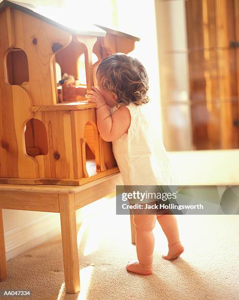 female toddler (12-15 months) playing with wooden doll house - doll house stockfoto's en -beelden