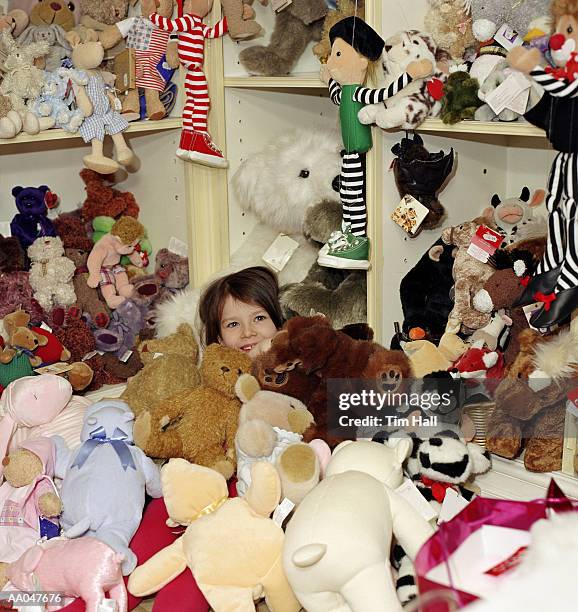 girl (4-6) in pile of stuffed animals in toy store, portrait - toy store stock pictures, royalty-free photos & images