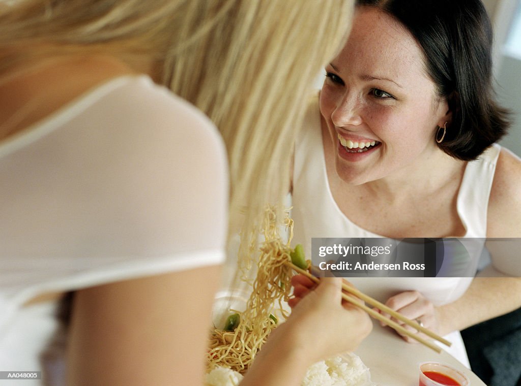 Two women eating noodles with chopsticks, elevated view