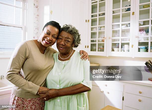 adult daughter hugging mother in kitchen - donna matura - fotografias e filmes do acervo