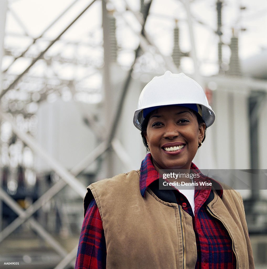 Woman wearing hard hat in front of power station, portrait