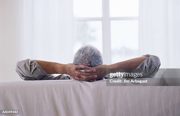 man relaxing on sofa with hands behind head,  rear view - man rear view grey hair closeup stock pictures, royalty-free photos & images