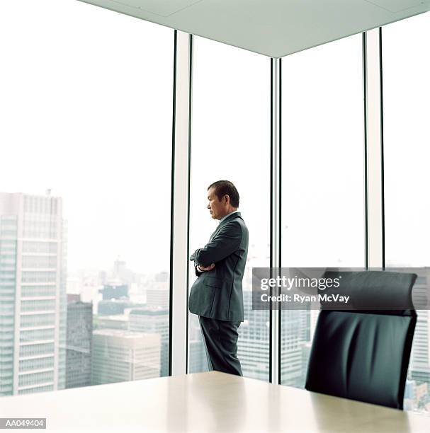 mature businessman looking out office window, side view - office skyscraper stock pictures, royalty-free photos & images