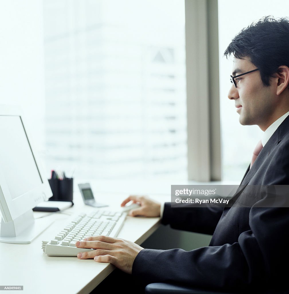 Businessman working on computer at desk in office, side view