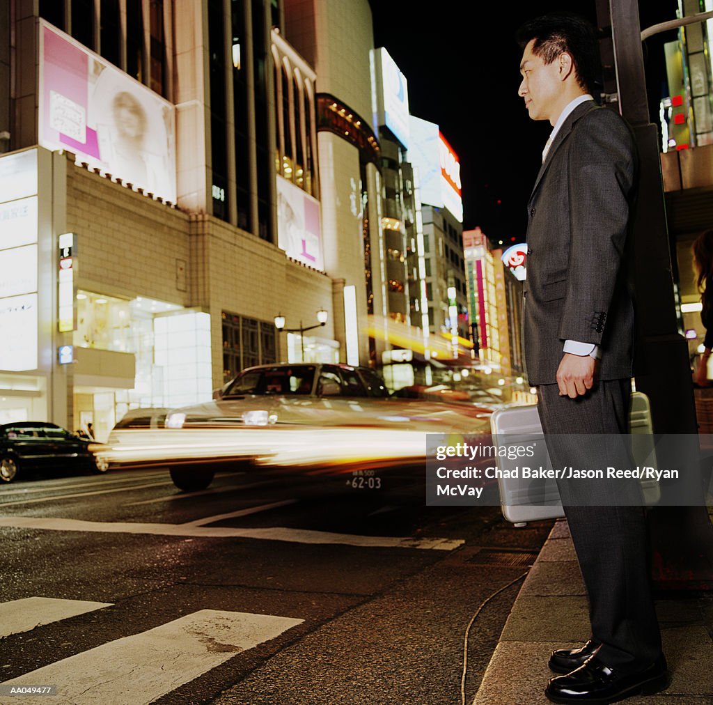 Businessman standing at busy crosswalk, night (blurred motion)