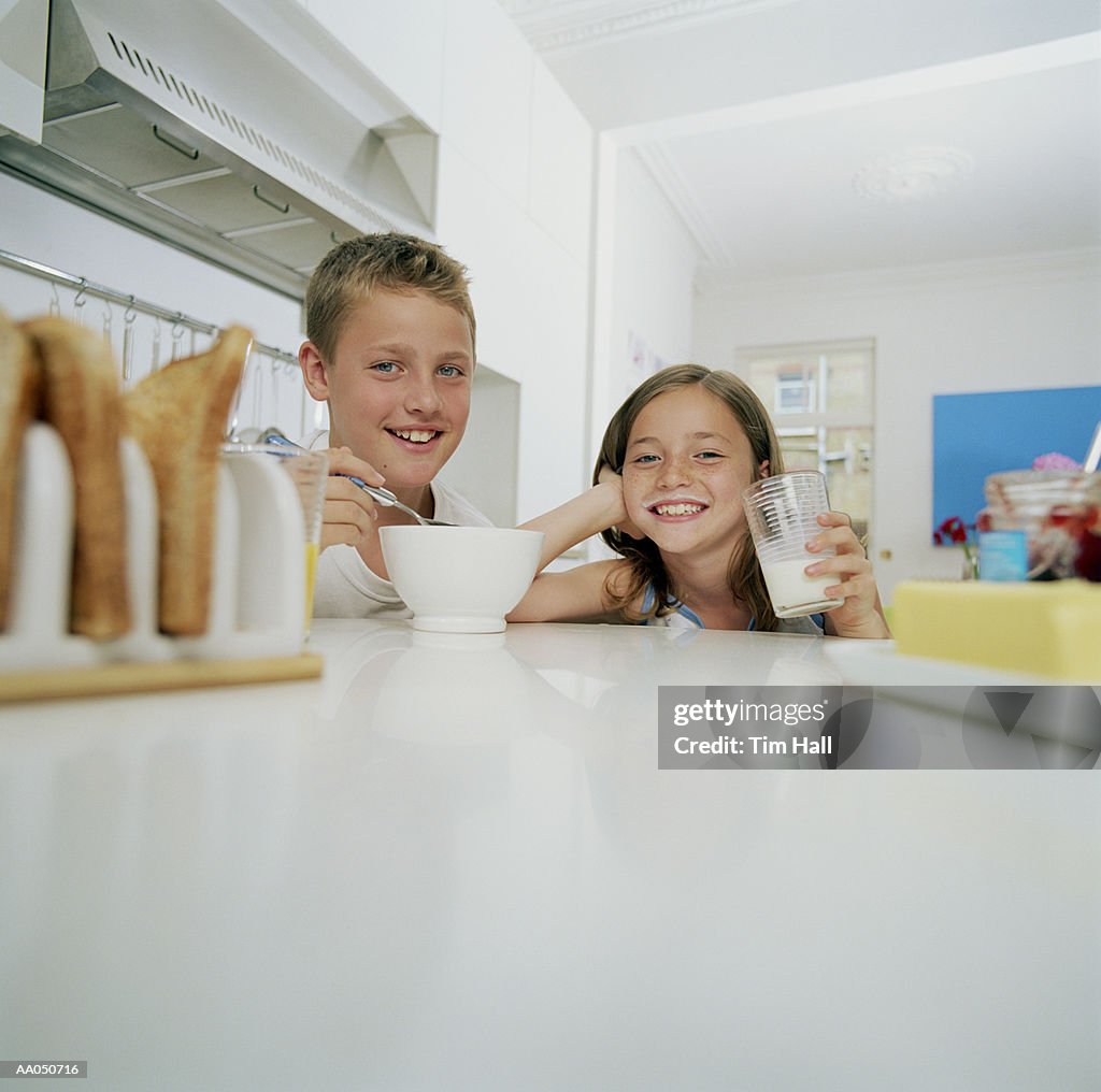 Brother and sister (10-12) having breakfast, smiling, portrait
