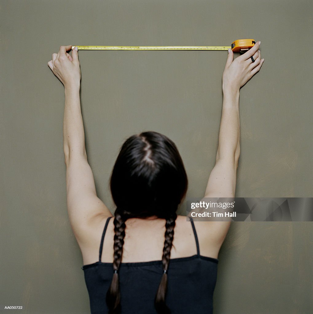 Woman holding tape measure against wall, rear view