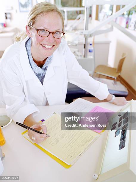 female dentist at desk with medical records, smiling, portrait - ficha-dentária imagens e fotografias de stock