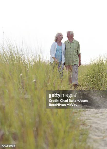 senior couple walking arm-in-arm in field toward beach - baker beach stock pictures, royalty-free photos & images