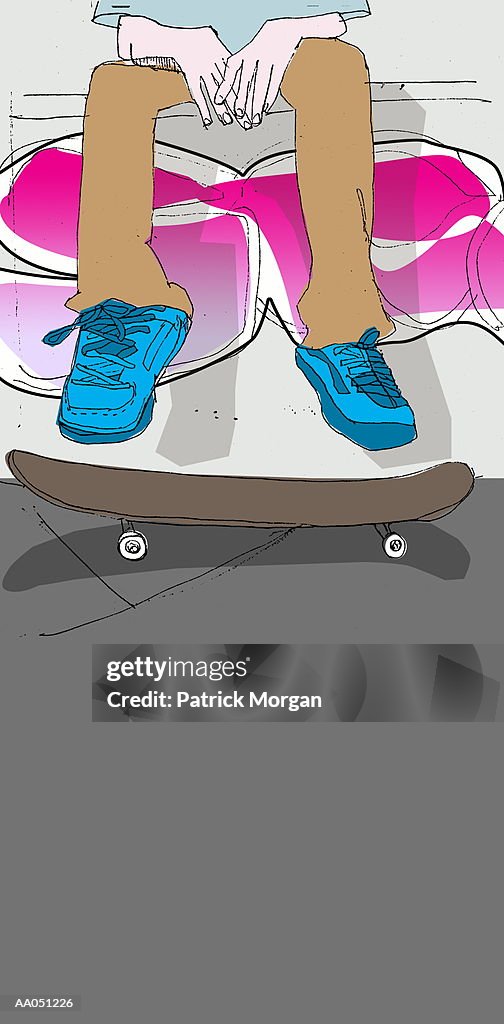Young man seated above skateboard, low section