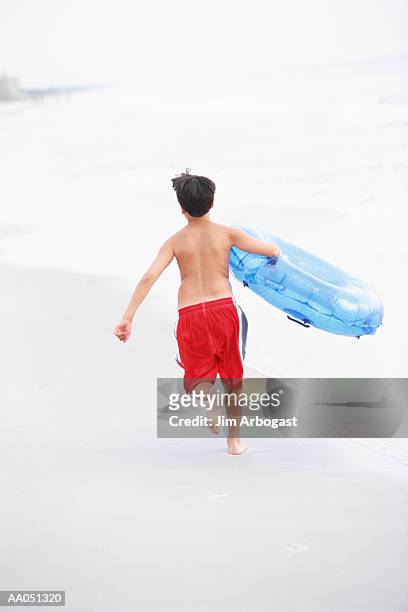 boy (10-12) running on beach, carrying inner tube, rear view - 1516 stock pictures, royalty-free photos & images