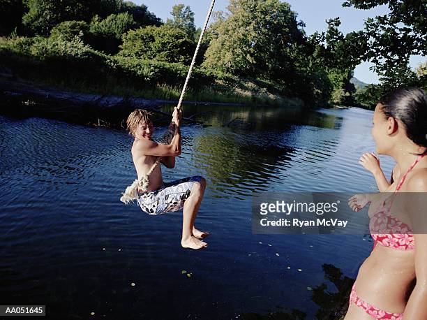 teen girl watching teen boy (14-16) on rope swing over water, summer - repgunga bildbanksfoton och bilder