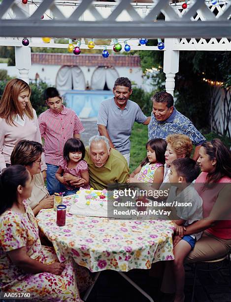 multi-generation family watching man blow out candles on cake - great granddaughter stock pictures, royalty-free photos & images