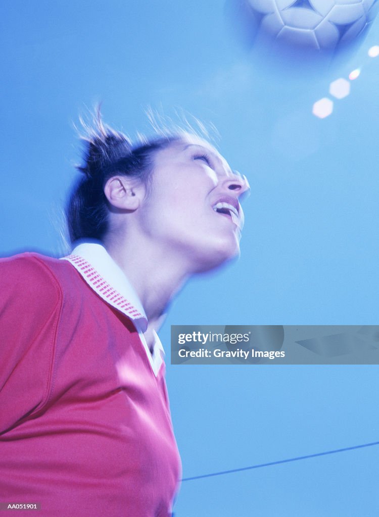 Female soccer player heading ball, low angle view (blurred motion)