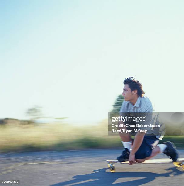 young man kneeling down on longboard, side view (blurred motion) - surfista de asfalto imagens e fotografias de stock