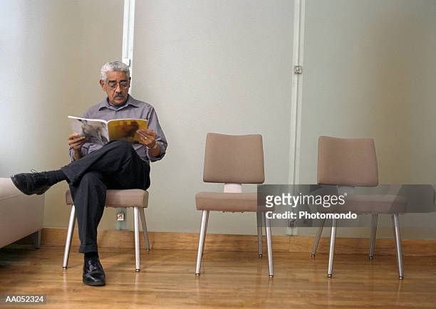 mature man reading magazine in waiting room - arztstuhl stock-fotos und bilder