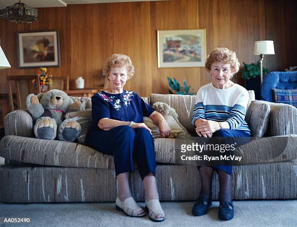 elderly twin sisters sitting on sofa, smiling, portrait - old livingroom stock-fotos und bilder