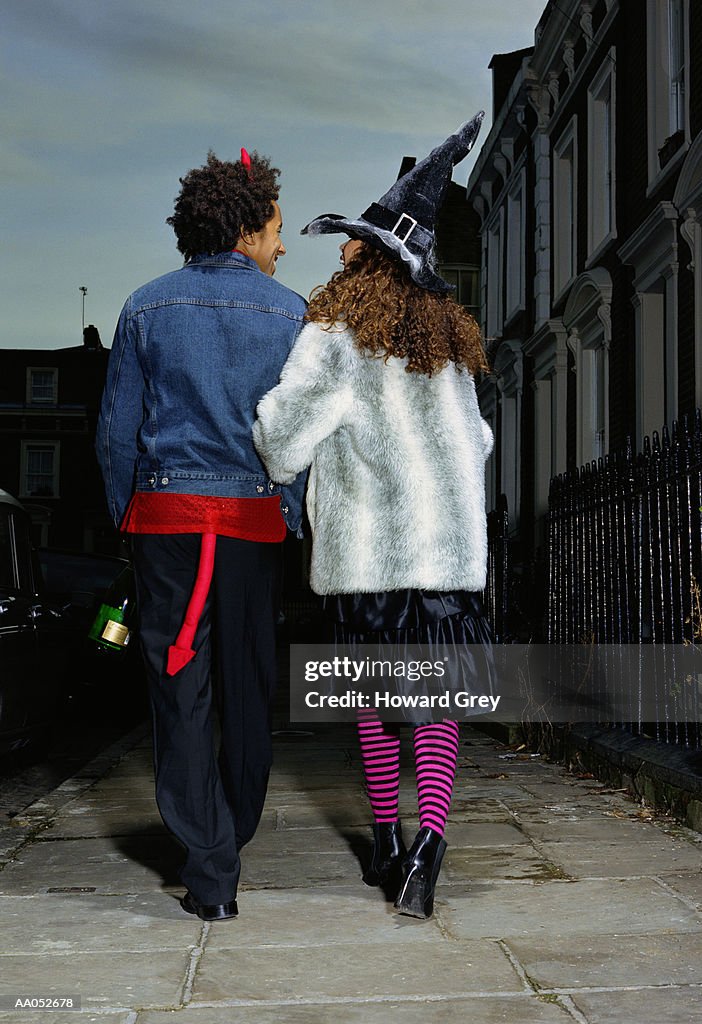 Couple dressed in costume walking arm in arm, rear view