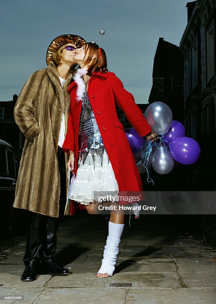Couple in costume kissing on sidewalk, low angle view