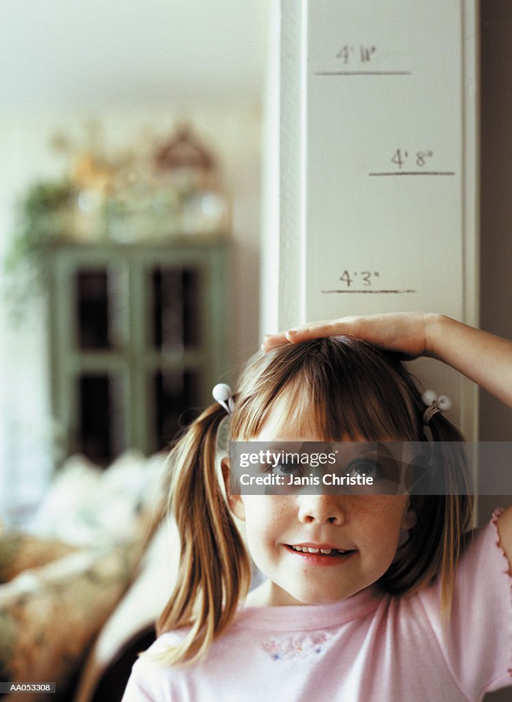 Young girl (6-8) measuring height on wall, high section
