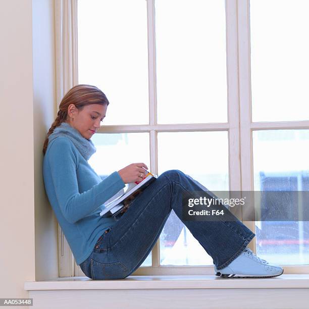 teenage girl (16-18) sitting on window sill, reading book, side view - f 16 stock pictures, royalty-free photos & images