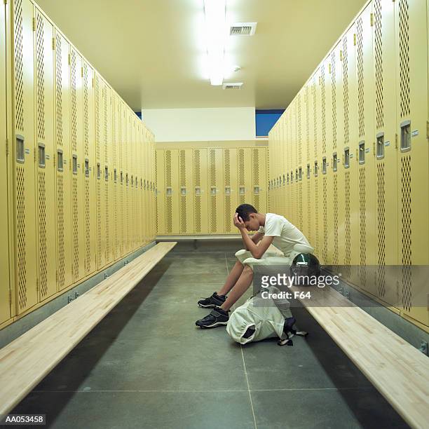 teenage boy (15-17) in football uniform, sitting in locker room - locker room ストックフォトと画像