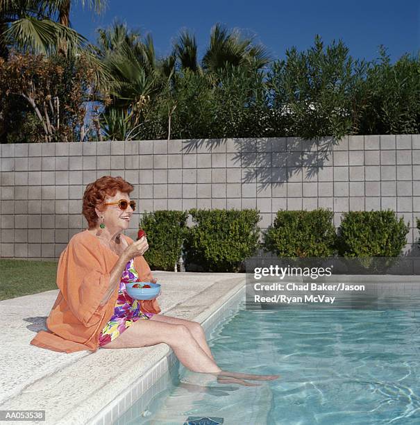 elderly woman sitting beside swimming pool, eating strawberries - old woman in swimsuit stock pictures, royalty-free photos & images