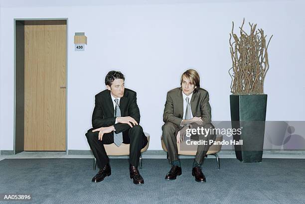 two businessmen sitting on chairs in hallway beside office door - taburete pequeño fotografías e imágenes de stock