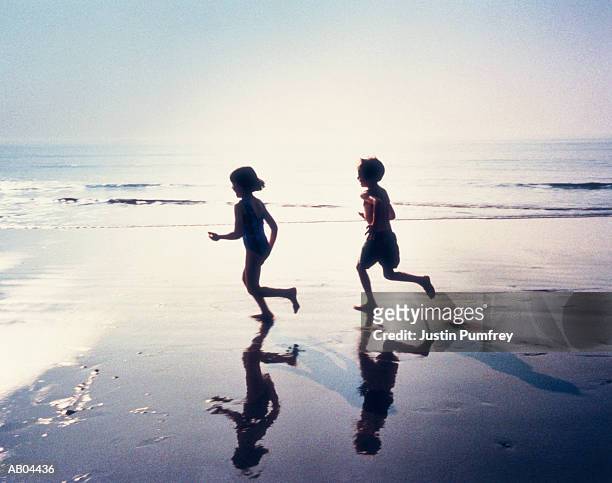 boy and girl in silhouette, running along the beach - silhouette mädchen rennen stock-fotos und bilder