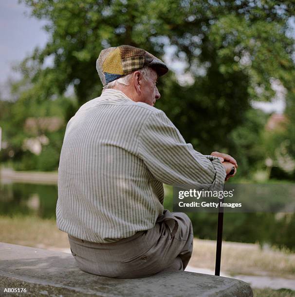 back view of elderly man, sitting on stone bench - gorra plana fotografías e imágenes de stock