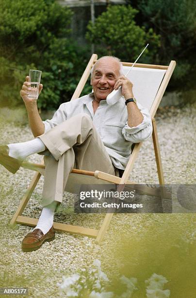 elderly man sitting in garden, using mobile phone - telefono fijo fotografías e imágenes de stock