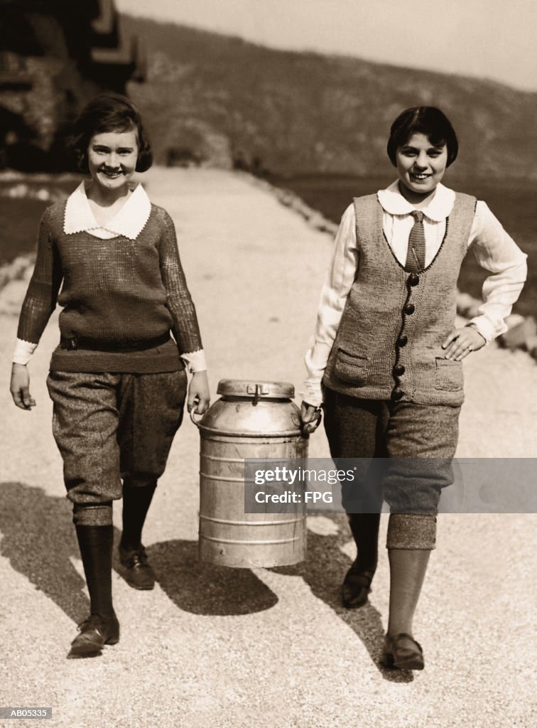 TWO TEENAGE GIRLS CARRYING A MILK CHURN / ARCHIVE SHOT