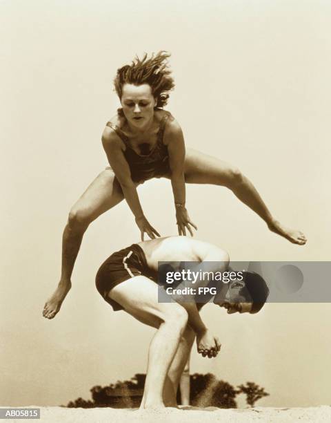 young couple playing leapfrog at beach (b&w sepia tone) - homme année 50 photos et images de collection