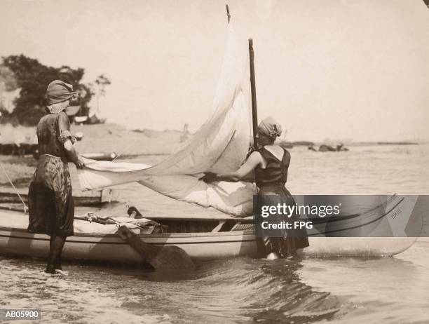 two women standing in water, adjusting boat's sail, rear view (b&w) - two toned dress stockfoto's en -beelden