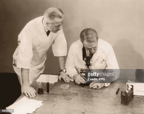 two men working in laboratory, one looking into microscope (b&w sepia) - archive 2005 stock-fotos und bilder