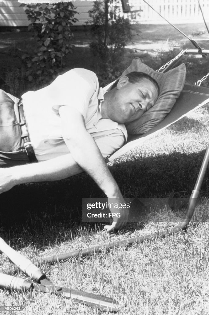 Man sleeping on cot in garden, hedge shears on lawn (B&W)