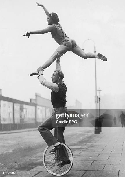 male acrobat on unicycle supporting woman in air (b&w) - acrobate photos et images de collection