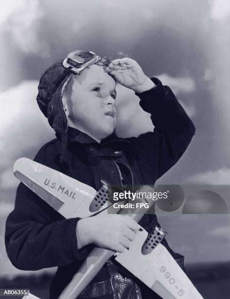 boy (8-10) wearing flying cap and goggles holding toy plane (b&w) - fliegermütze stock-fotos und bilder