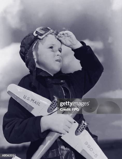 boy (8-10) wearing flying cap and goggles holding toy plane (b&w) - aviation hat stock pictures, royalty-free photos & images